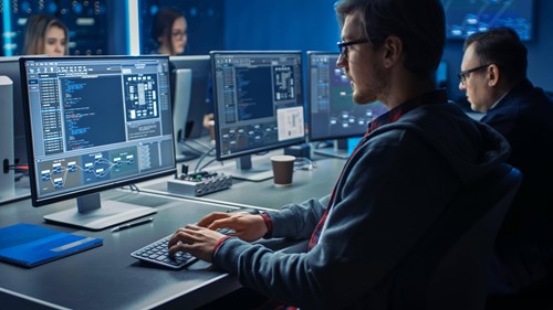 man in glasses typing on computer with analytical data showing on the screen 